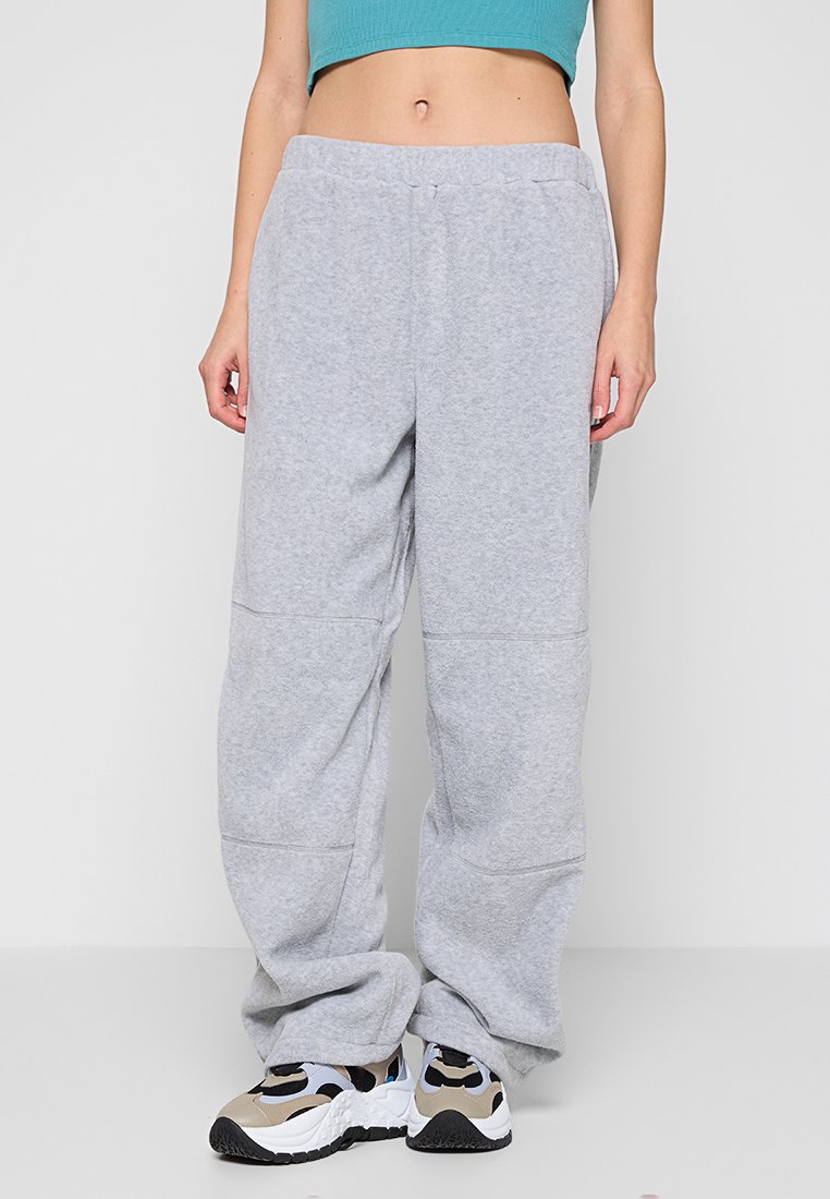 Grijze sweatpants van zacht materiaal, met een losse pasvorm, elastische tailleband en zichtbare stiksels. Gemaakt in combinatie met kleurrijke sneakers.