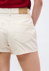 Λευκά τζιν σορτς με πίσω τσέπες, φορεμένα από ένα άτομο που φοράει κόκκινη υφασμάτινη μπλούζα, εμφανίζοντας τη μέση και την περιοχή πάνω από τους μηρούς.