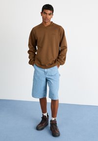 Brun genser med v-hals, lyseblå denimshorts, brune tursko. Glatt tekstur, avslappet passform, uformell stil.