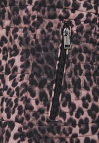 Gros plan d'un tissu matelassé imprimé léopard avec une fermeture éclair noire et un tirette argentée portant la marque "GUESS" sur le côté droit.