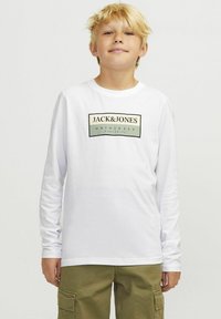 Balta ilgomis rankovėmis marškinėliai su juodu ir žaliu stačiakampiu logotipu, kuriame užrašyta "JACK&JONES ORIGINALS" priekyje. Minkšta tekstūra.