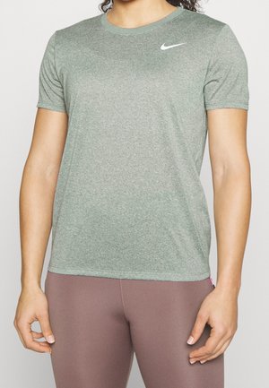 Personne portant un t-shirt gris Nike à manches courtes et des leggings mauve, vue du cou jusqu'aux hanches sur un fond clair uni.