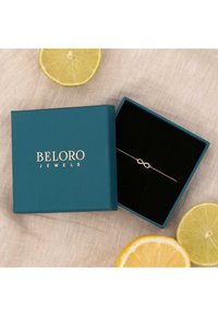 Türkise Schmuckbox mit goldener Schrift enthält ein zartes Armband aus Roségold mit einem Unendlichkeitssymbol auf einem schwarzen Kissen.