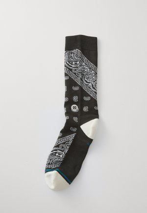 Black sock with white paisley pattern, contrasting white toe and heel, ribbed cuff, and teal accent near the base.