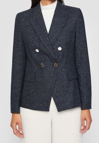 Marinblå dubbelknäppt blazer i texturerat tyg, med två stora silverknappar, sidofickor och en skräddarsydd passform.