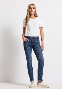 Bílá tričko s krátkým rukávem v kombinaci s modrými džíny. Džíny mají rovný střih a jemné vyblednutí, s ohrnutými nohavicemi a kapsami.