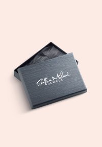 Gråt smykkeskrin med tekstureret overflade, med hvidt logo "Sofia Milani JEWELS" på låget, delvist åbent for at afsløre sort foring.