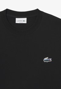 Camiseta de algodón negra de cuello redondo con un pequeño logo bordado en colores del cocodrilo de Lacoste en la parte izquierda del pecho. Corte clásico.