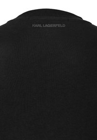 Tissu noir avec un subtil texte "KARL LAGERFELD" imprimé près de la nuque, en haut du dos.