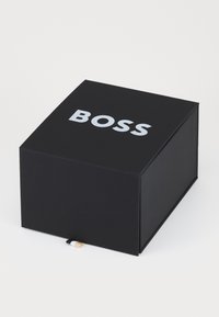 Juodas stačiakampis dėžutė su matinio paviršiaus apdaila, viršuje pabrėžta balta "BOSS" logotipu ir maža daugiapakopė spalvota juostele, skirta traukti.