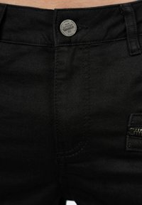 Jeans in denim neri con una vestibilità classica, caratterizzati da una chiusura con bottone argentato, dettagli con tasche con zip e cuciture a vista.