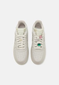 Baskets en cuir beige clair avec une boîte à orteils perforée, des lacets plats et des accents décoratifs en rose et vert sur les lacets.