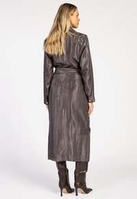Lang, grijze satijnen jurk met een gladde textuur, knoopmanchetten en een ceintuur op de taille. Gecombineerd met kniehoge, getextureerde bruine laarzen.