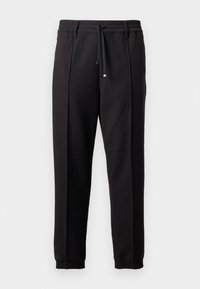Pantaloni negri cu un brâu, șnur și manșete elastice. Prezintă pliuri și un material neted, texturat.