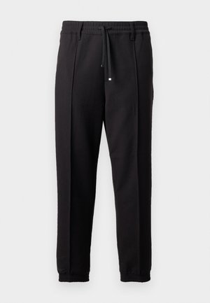 Sorte bukser med liv, snor og elastiske mansjetter. Har plisséer og et glatt, teksturert stoff.