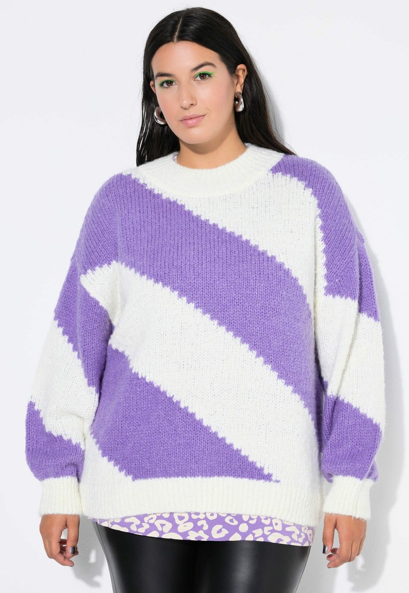 Strickpullover mit übergroßer Silhouette; verfügt über ein auffälliges lila und weißes Zickzackdesign. Weicher Stoff und gerippte Bündchen. Über einem Leopardenmuster-Shirt getragen.