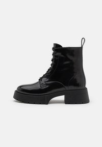 Zwarte enkellaarzen van lakleer met een dikke zool, ronde neus en vetersluiting; voorzien van een treklus aan de achterkant voor gemakkelijk aan- en uittrekken.