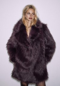 Burgundowa kurtka z sztucznego futra o grubej, teksturowanej powierzchni, z szerokimi klapami i luźnym, oversize'owym krojem.