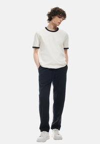 Witte T-shirt met een marineblauwe geribbelde kraag en manchetten, gecombineerd met zwarte broek en witte sneakers, met een relaxed fit en een zachte textuur.