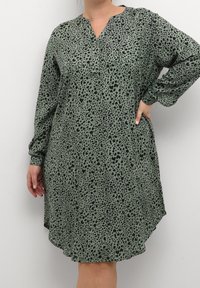 Vestido verde con estampado de leopardo, de manga larga, escote en V, forma fluida y con bolsillos; hecho de un tejido ligero y texturizado.