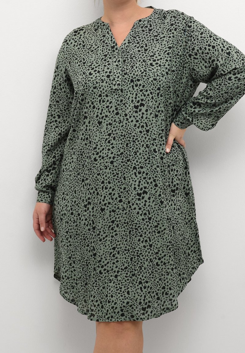 Vestido verde con estampado de leopardo, de manga larga, escote en V, forma fluida y con bolsillos; hecho de un tejido ligero y texturizado.