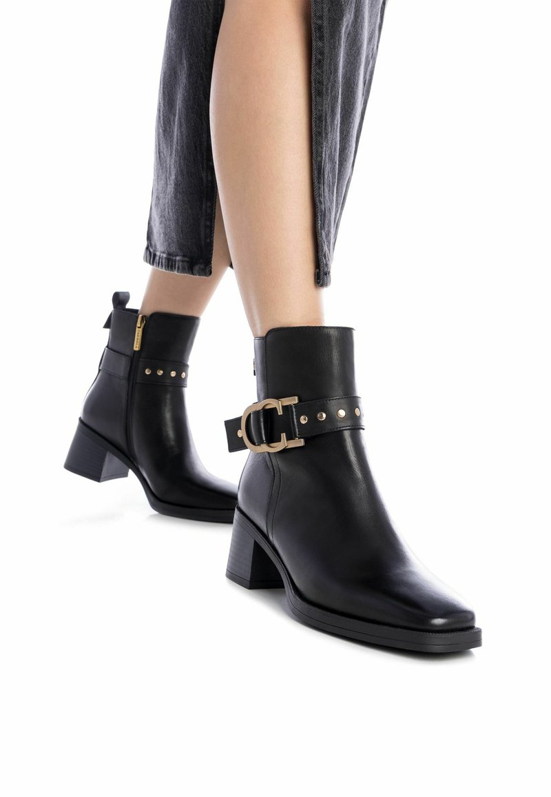 Botas de cuero negras hasta el tobillo con punta cuadrada, tacón bloque, detalles en dorado y una correa decorativa con tachuelas. Detalles de textura sutil.