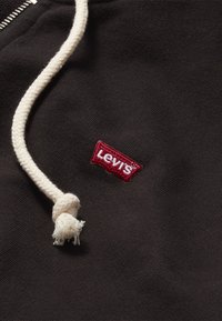 Zwarte hoodie met een gevlochten crèmekleurige trekkoord, voorzien van een klein rood geborduurd Levi's-logo in de rechterbovenhoek. Zacht katoenen stof.