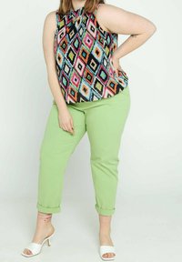 Färgglad ärmlös topp med ett diamantmönster i svart, rosa, blått, grönt och orange, som kombineras med ljusgröna upprullade byxor och vita klackar.