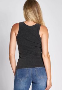 Black ribbed tank top with a fitted design and wide shoulder straps, paired with blue denim jeans, viewed from the back.
