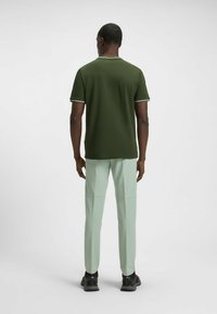 Dark green short-sleeve shirt with white trim; paired with light green slim-fit pants and black athletic shoes. Smooth fabric texture.