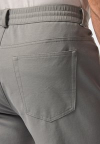 Grå tygbyxor har en slät yta, resårmidja och en bakficka med en broderad detalj i form av ett berg.