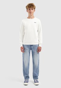 Witte sweatshirt met ribgebreide boorden, voorzien van een klein blauw logo. Gecombineerd met lichtblauwe rechte jeans en blauwe sneakers. Eenvoudig ontwerp.