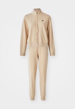 Bežiki äkkipukud pehmest kangast, millel on kõrge krae, soonikkoes mansetid ja diskreetne logo rinna ja pükste peal.