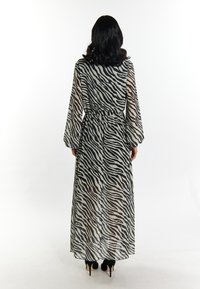 Maxikleid aus durchscheinendem Chiffon mit einem schwarz-weißen Zebra-Druck; verfügt über lange Ärmel und einen Taillengürtel, kombiniert mit schwarzen Absätzen.