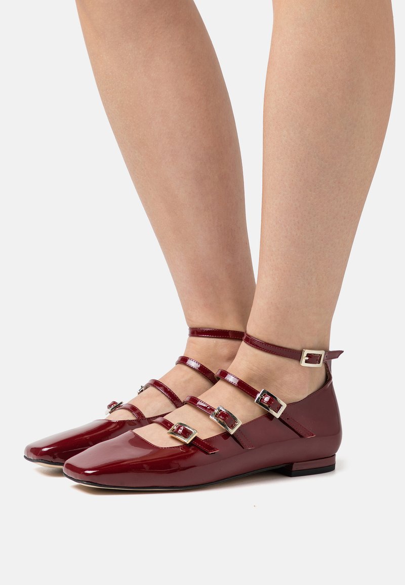Rote Lackleder-Ballerinas mit spitz zulaufender Zehenpartie, ausgestattet mit drei Riemen und silbernen Schnallenakzenten. Niedriger Absatz und glatte Textur.