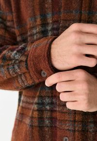 Brown and blue plaid flannel shirt with a soft texture, featuring a buttoned cuff and a relaxed cut.