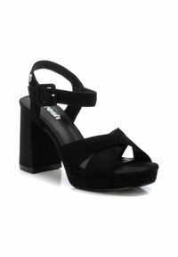 Sandalias de tacón alto de ante negro con un grueso tacón cuadrado, diseño de tiras entrelazadas y correa para el tobillo ajustable con un hebilla de metal.