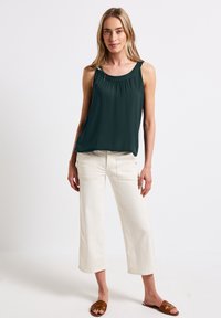 Top senza maniche verde scuro con scollo arricciato, abbinato a pantaloni a gamba larga crema con tasche applicate e sandali scivolati marroni.