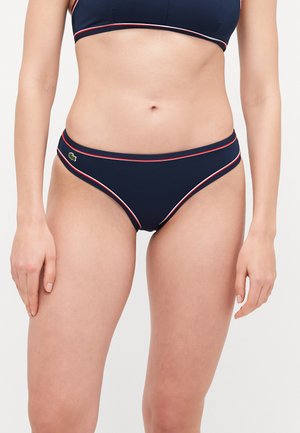Navy bikinihousut punaisilla ja valkoisilla korostusviivoilla, joissa on matala vyötärödesign ja pieni logo vasemmalla lantiossa. Sileä materiaali.