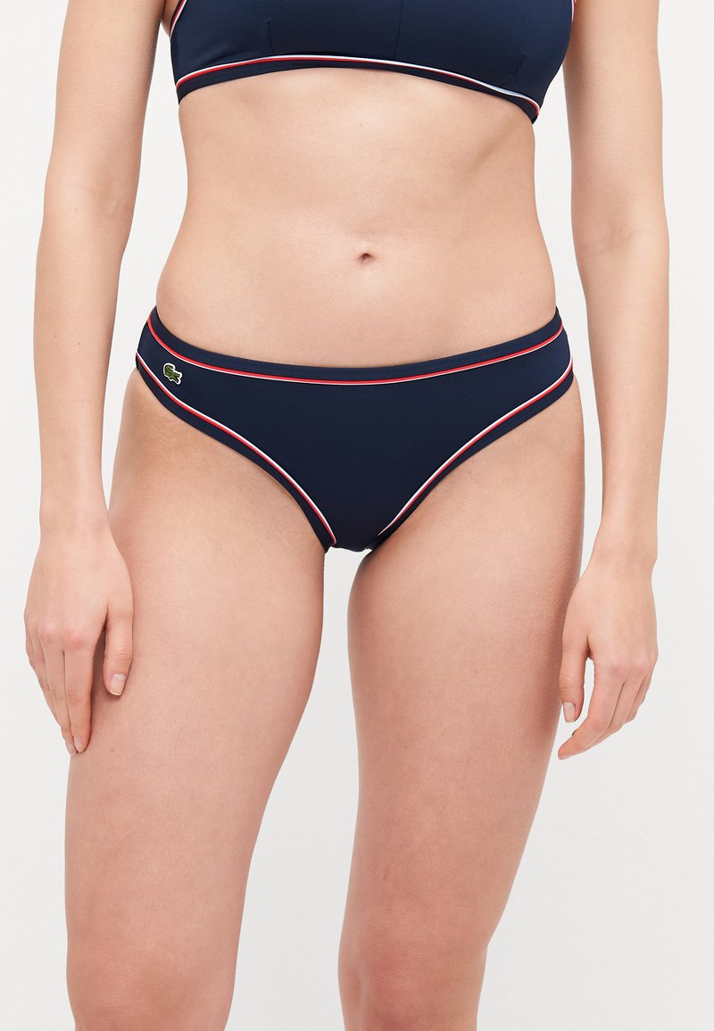 Jūras spēku bikini apakša ar sarkaniem un baltiem akcentiem, ar zemu jostasvietu un mazu logo kreisajā gurnā. Gluda materiāla.