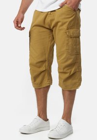 Shorts cargo kaki avec une coupe décontractée, longueur genou, plusieurs poches et un matériau en mélange de coton durable. Assortis à des baskets blanches.
