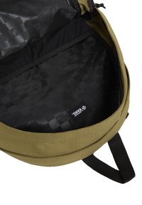 Olivgrön ryggsäck inuti med ett svart rutmönster, med en Vans-logotagg. Tyget ser mjukt och hållbart ut.