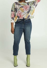 Top de punto ligero con estampado floral y corte holgado, combinado con vaqueros azules y botines verdes brillantes.