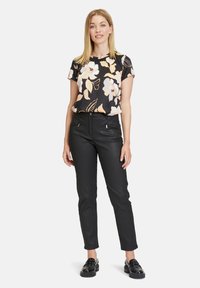 Schwarze Blumenshirt mit kurzen Ärmeln, verziert mit hellen Blumen; kombiniert mit schmalen schwarzen Hosen und schwarzen klobigen Loafers.