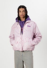 Light pink jacket with a pattern of pink outlines. Features a zip front, side pockets, and elastic band at the hem. Worn over a purple hoodie.