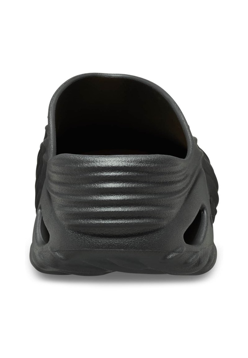 Calzado negro con parte trasera redondeada, textura suave, diseño estriado en el tacón y agujeros de ventilación a los lados.