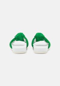 Sandales en daim vert avec des brides croisées, semelle blanche et détails de texture subtils. Conçues pour le confort et la facilité de port.