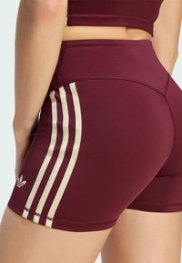 Close-up of a person wearing maroon athletic shorts with three beige stripes and an Adidas logo on the side.
