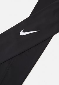 Zwarte sportleggings van gladde, rekbare stof. Met een wit Nike-logo aan de linkerkant en platte naden voor extra comfort.