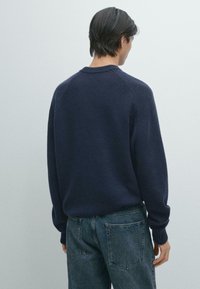 Marineblauer Strickpullover mit Rundhalsausschnitt und Raglanärmeln, kombiniert mit ausgewaschenen Denim-Jeans. Weiche Textur und bequeme Passform.